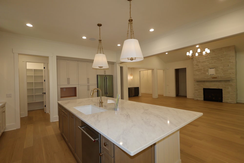 Large kitchen island with marble countertop and sink, open to living room with stone fireplace and hardwood floors