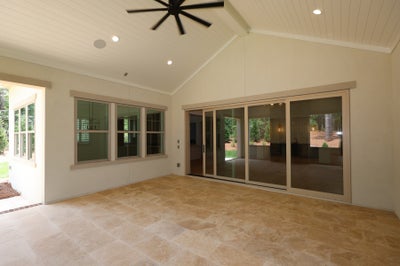 Covered patio with vaulted ceiling, ceiling fan, tile floor, and large sliding glass doors leading to backyard