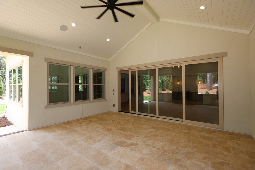 Covered patio with vaulted ceiling, ceiling fan, tile floor, and large sliding glass doors leading to backyard
