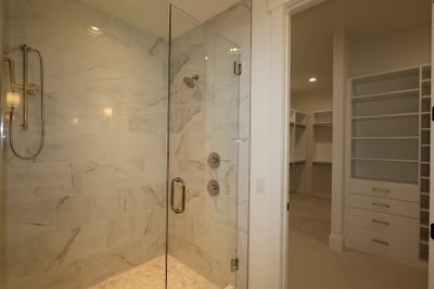 Walk-in shower with marble tile walls and glass door, adjacent to a large walk-in closet with built-in shelving and drawers.