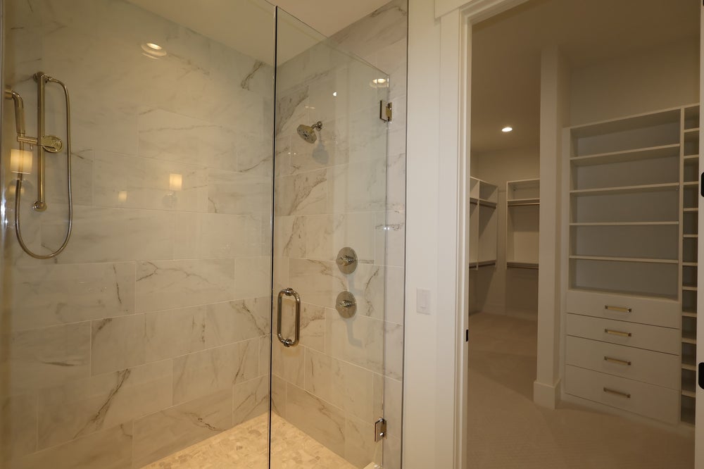 Walk-in shower with marble tile walls and glass door, adjacent to a large walk-in closet with built-in shelving and drawers.