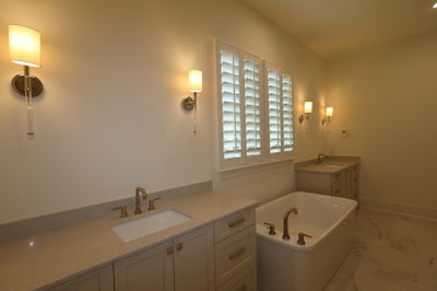 Bathroom with soaking tub, dual vanities, marble floors, and plantation shutters with wall sconces