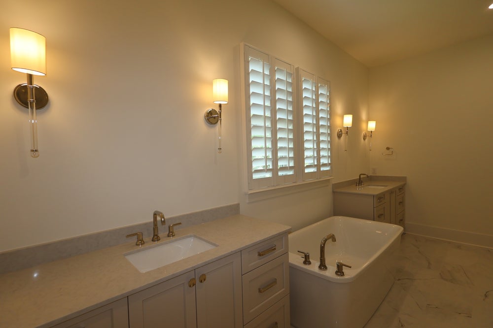Bathroom with soaking tub, dual vanities, marble floors, and plantation shutters with wall sconces