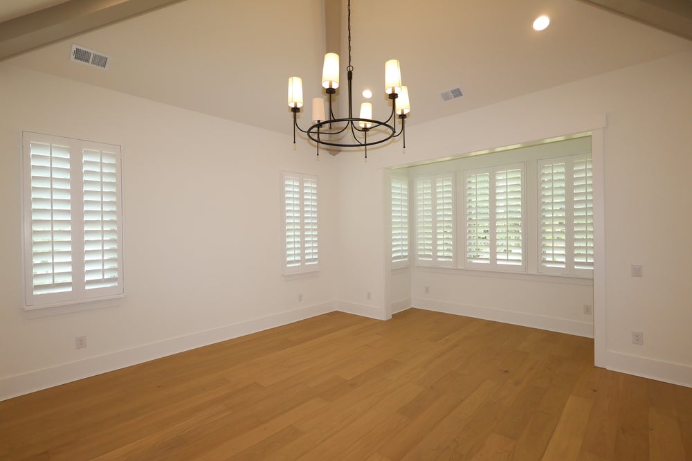 Empty room with vaulted ceiling, hardwood floors, chandelier, and white plantation shutters on multiple windows