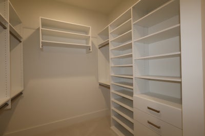 Walk-in closet with white built-in shelving, hanging rods, and two drawers