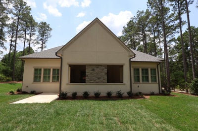Single-story home with stucco exterior, stone accent, green shutters, and tall pine trees in background