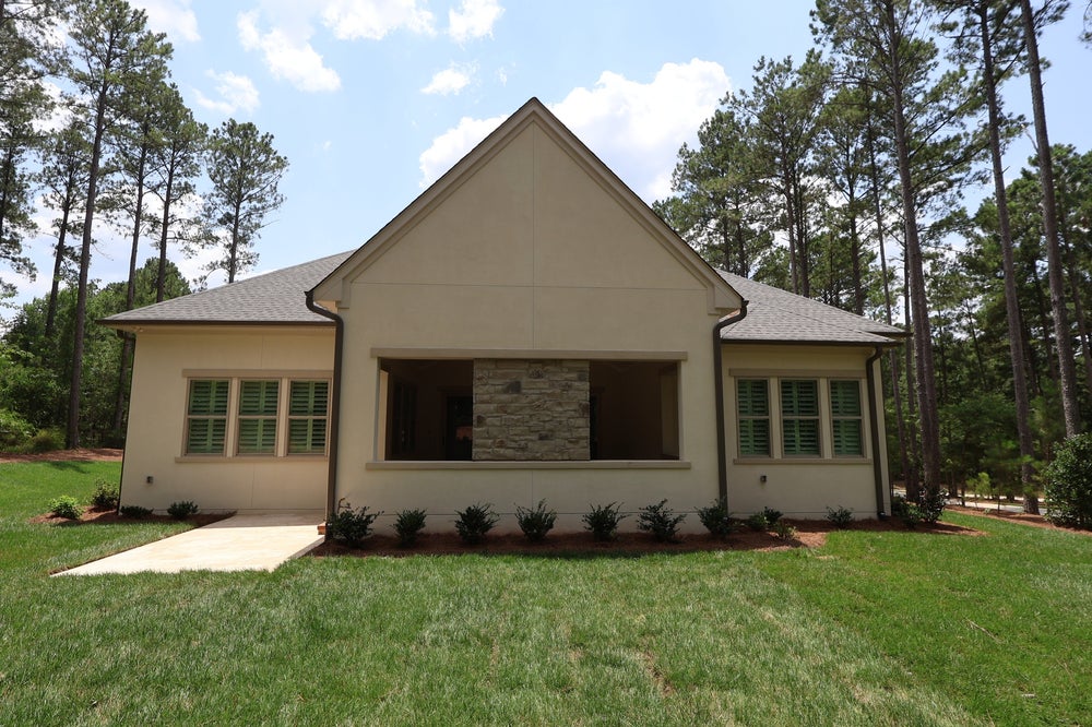 Single-story home with stucco exterior, stone accent, green shutters, and tall pine trees in background