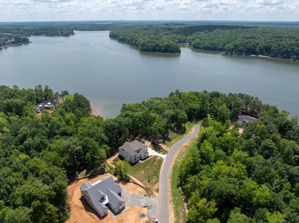 Aerial view of two new homes under construction on wooded lots near a large lake surrounded by trees