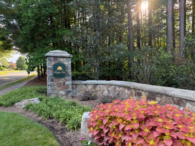Hadley Park neighborhood entrance with stone pillar sign, low stone wall, and colorful landscaping near wooded area
