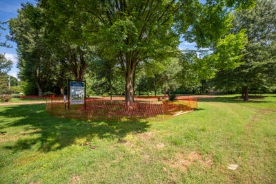 Vacant lot with orange safety fencing, large trees, and a builder's available homes sign
