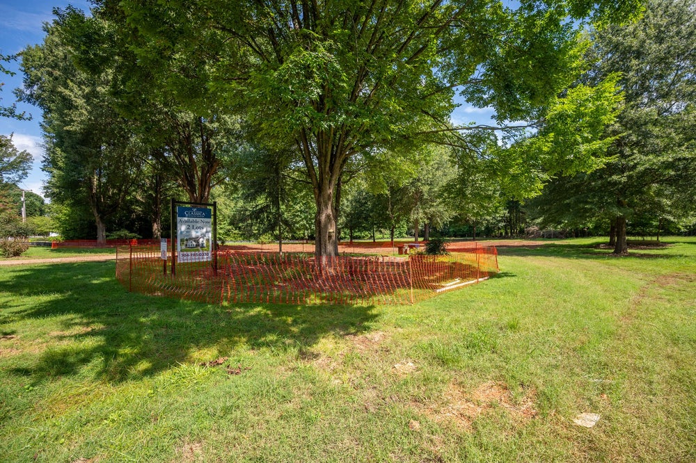 Vacant lot with orange safety fencing, large trees, and a builder's available homes sign