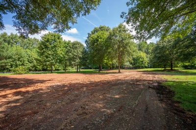 Cleared and graded dirt lot surrounded by mature trees, ready for construction