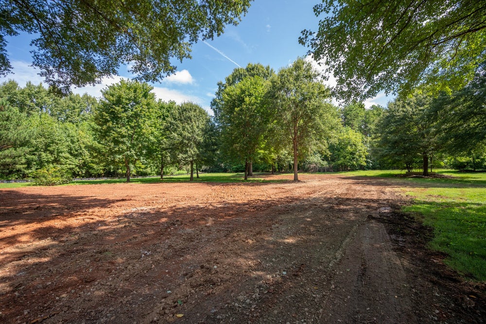 Cleared and graded dirt lot surrounded by mature trees, ready for construction
