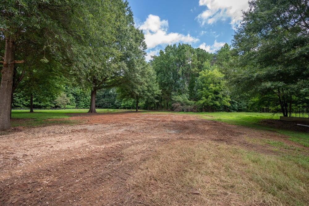 Vacant lot with cleared dirt area, mature trees, and green grass along the edges