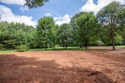 Cleared and graded building lot with red clay soil surrounded by mature trees and green grass