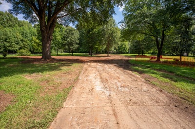 Cleared dirt lot with mature trees, grass edges, and orange construction fencing in background