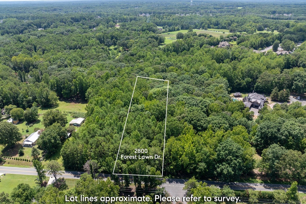 Aerial view of wooded vacant lot at 2800 Forest Lawn Dr with approximate lot lines marked, surrounded by trees and nearby homes.