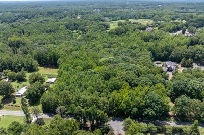 Aerial view of wooded land parcel with scattered homes and a road along the front edge.