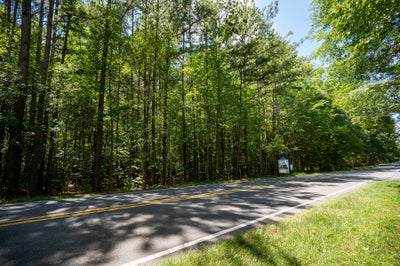 Two-lane road bordered by tall green trees and a small community sign on the right side
