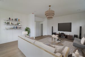 Living room with wall-mounted TV, built-in shelves, neutral sectional sofa, and woven pendant light over glass coffee table