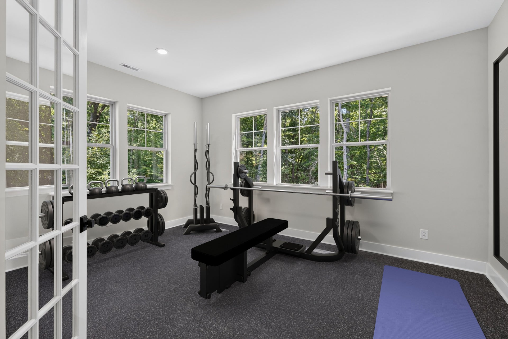 Home gym with bench press, dumbbell rack, kettlebells, and yoga mat on dark carpet flooring