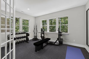Home gym with bench press, dumbbell rack, kettlebells, and yoga mat on dark carpet flooring