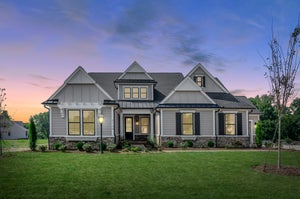 Craftsman-style home with gray board-and-batten siding, stone foundation, covered porch, and large windows at dusk