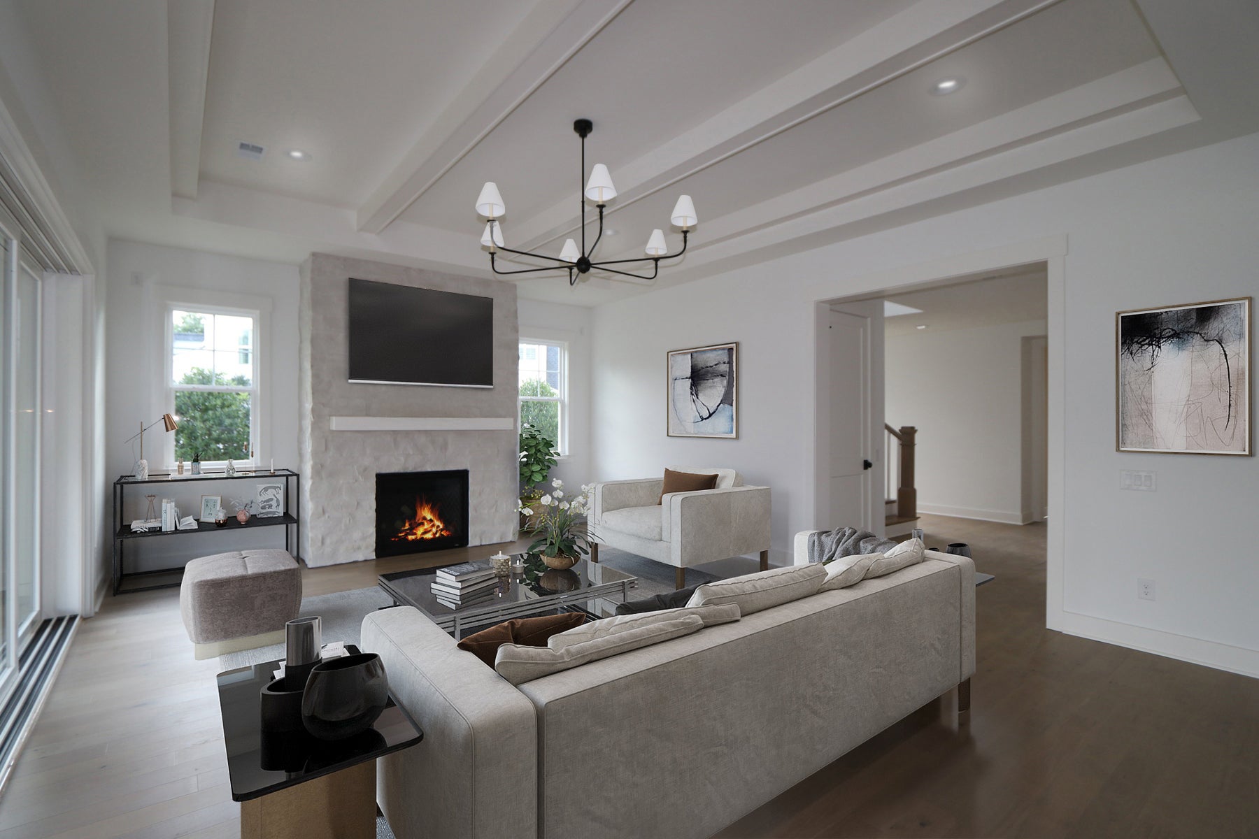 Living room with stone fireplace, wall-mounted TV, tray ceiling, and neutral furniture with modern chandelier