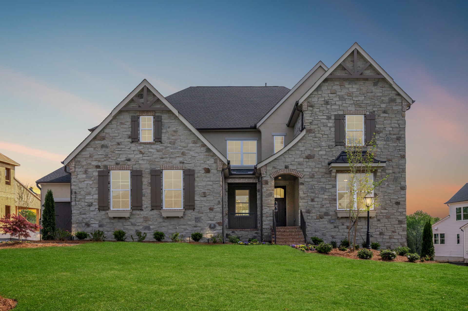Two-story stone home with dark shutters, arched entry, and manicured front lawn at dusk