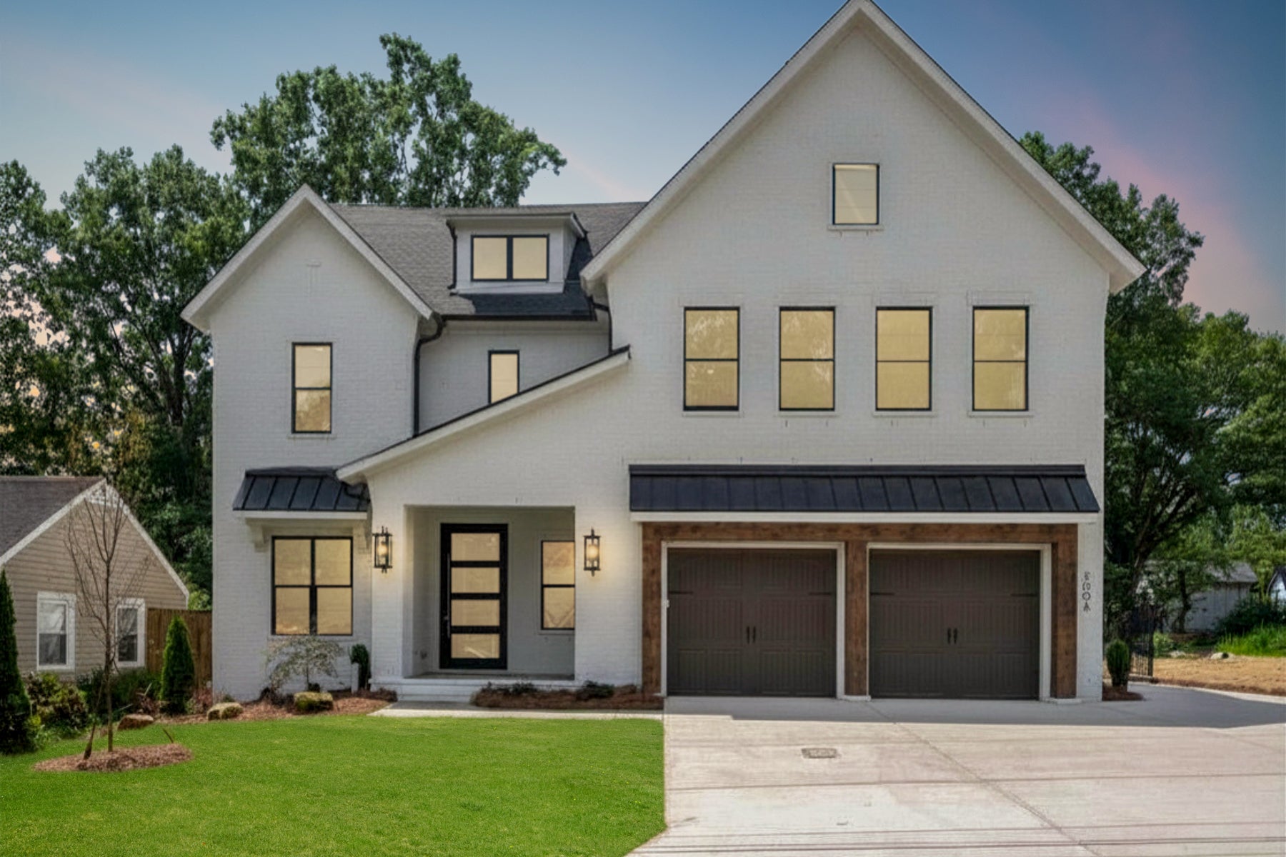Two-story white brick home with black metal roof, two-car garage, and green front lawn