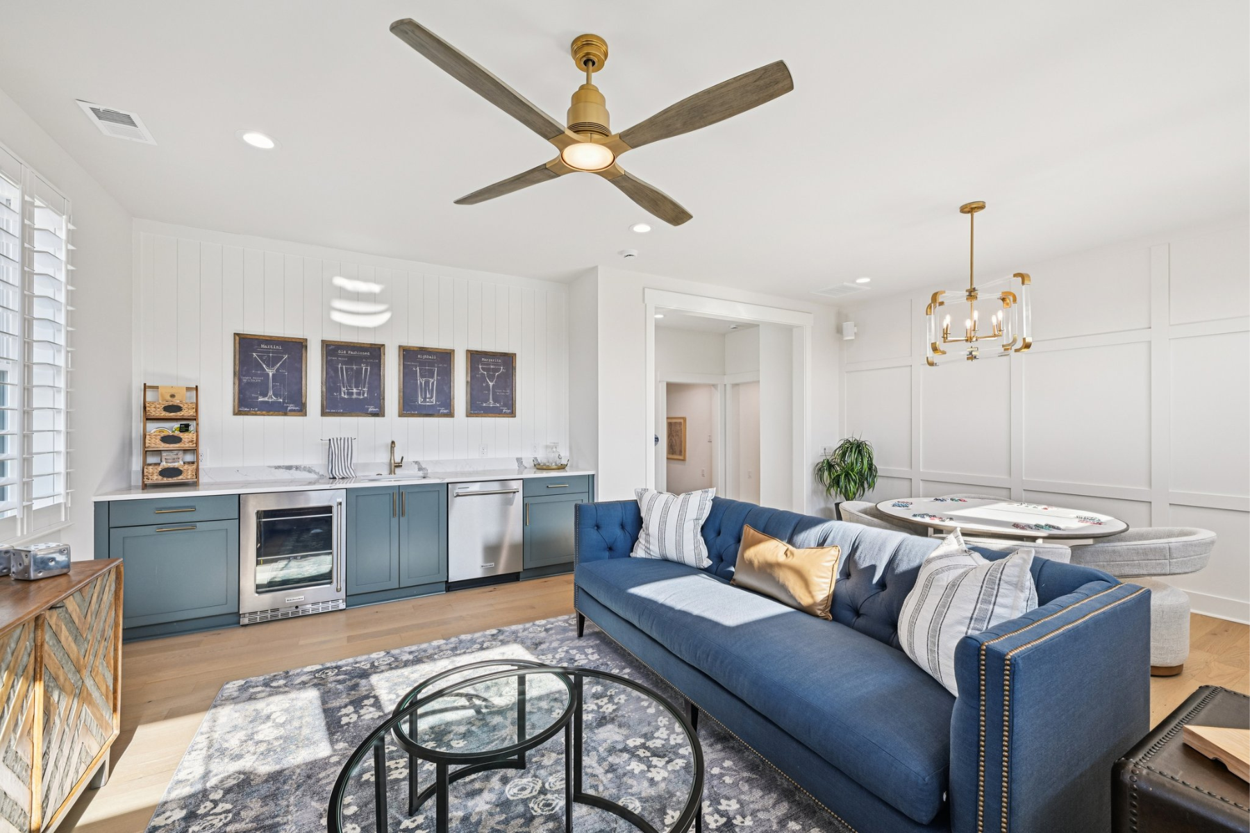 Living room with blue sofa, wet bar with teal cabinets, hardwood floors, and ceiling fan