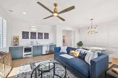 Living room with blue sofa, wet bar with teal cabinets, hardwood floors, and ceiling fan