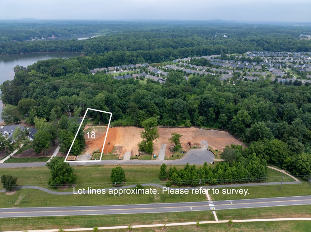 Aerial view of lot 18, a cleared residential building lot near a lake and wooded neighborhood subdivision.