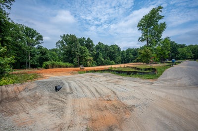 Cleared and graded residential building lot with red clay soil, construction equipment, and surrounding trees