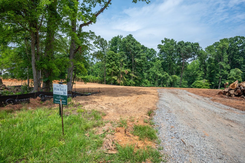 Vacant lot for sale with gravel driveway, cleared land, and wooded tree line in background