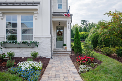 Home entrance with gray front door, brick walkway, flower beds, and American flag at address 2032