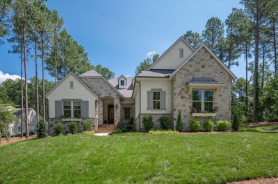 Two-story home with stone and stucco exterior, gray shutters, arched entry, and manicured front lawn surrounded by tall pine trees.