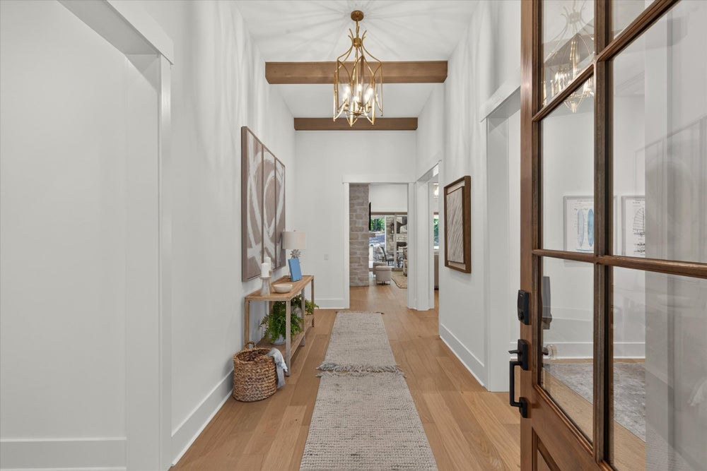 Bright entryway with wood beam ceiling, gold chandelier, hardwood floors, and glass-panel front door