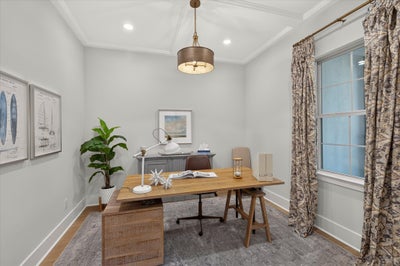 Home office with wood desk, pendant light, crown molding, and large window with patterned curtains