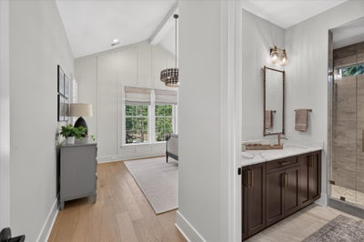 Master bathroom with dark wood vanity and marble countertop, adjoining bedroom with vaulted ceiling and hardwood floors