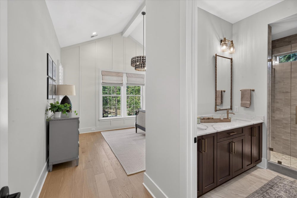 Master bathroom with dark wood vanity and marble countertop, adjoining bedroom with vaulted ceiling and hardwood floors