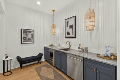 Wet bar with navy cabinets, marble countertop, wine fridge, and gold pendant lights on shiplap wall