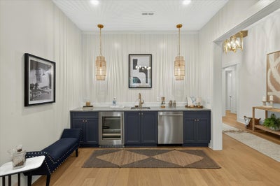 Wet bar with navy cabinets, wine fridge, sink, and gold pendant lights on shiplap wall with hardwood floors
