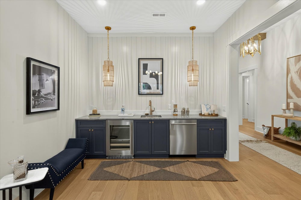 Wet bar with navy cabinets, wine fridge, sink, and gold pendant lights on shiplap wall with hardwood floors
