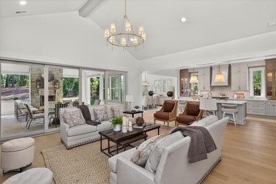 Open-concept living room with vaulted ceiling, chandelier, hardwood floors, and sliding doors to outdoor patio