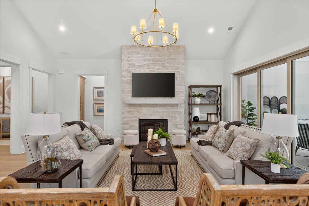 Living room with stone fireplace, wall-mounted TV, two neutral sofas, and a gold chandelier on vaulted ceiling