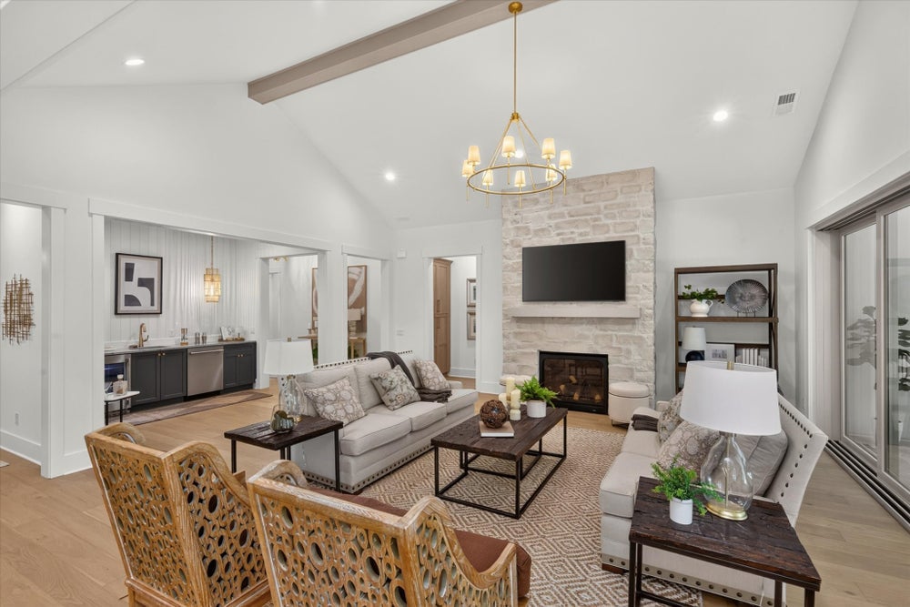 Open living room with vaulted ceiling, stone fireplace, chandelier, and hardwood floors open to kitchen