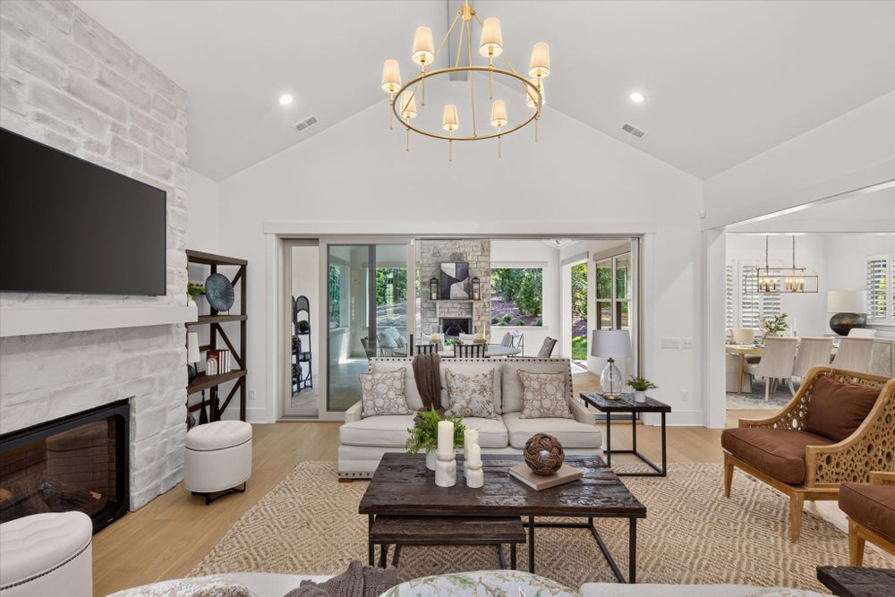Living room with vaulted ceiling, stone fireplace, gold chandelier, and sliding doors to outdoor patio