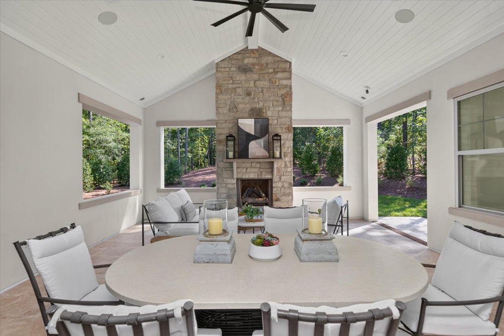 Covered outdoor patio with stone fireplace, dining table, seating area, vaulted ceiling, and ceiling fan