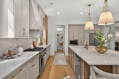 Large kitchen with white and gray cabinets, marble island, gas range, and gold pendant lights over hardwood floors